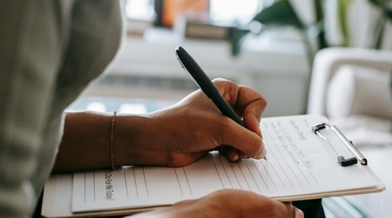 crop ethnic psychologist writing on clipboard during session